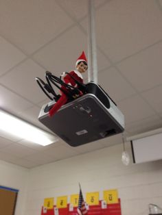 the elf is hanging from the ceiling in the classroom with his feet on the box