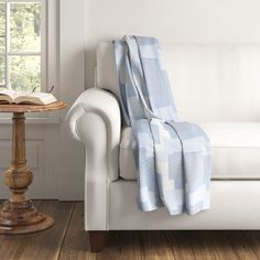 a white couch with a blue blanket on top of it next to a table and window