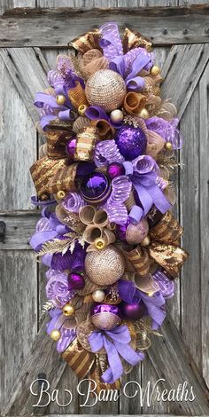 a purple and gold christmas wreath hanging on a wooden door with ornaments around it in the shape of bells