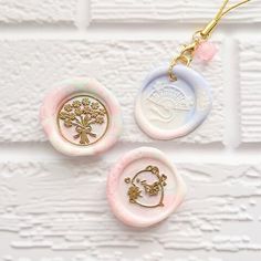 three different colored buttons are hanging on a white brick wall, one has a tree and the other has a gold - plated charm