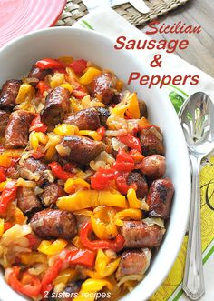 a bowl filled with sausage and peppers on top of a table next to silverware