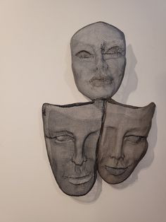 three masks with faces made out of mesh hanging on the wall in front of a white wall