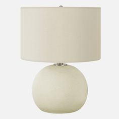 a white table lamp with a beige shade on the base and a light bulb attached to it