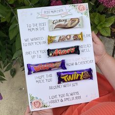 a person holding up a sign with candy on it and some flowers in the background