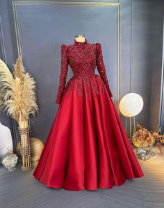 a red evening gown on display in front of a white vase with flowers and plants