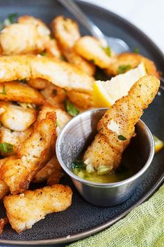 a plate full of fried food with dipping sauce on the side and lemon wedges