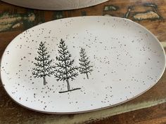 a white plate with black trees on it sitting on top of a wooden table next to a potted plant