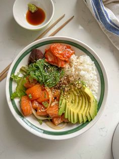 a bowl filled with rice, salmon and avocado on top of a table