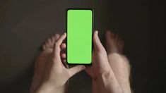 a person holding a cell phone with a green screen in their hands on a dark background