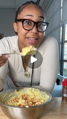 a woman is holding a spoon with food in it and looking at the camera while she eats