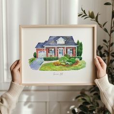 a person holding up a painting with a house in the background and plants behind it