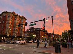 people are standing on the street corner waiting for the traffic light to turn green at sunset