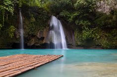 there is a wooden raft floating in the water next to a waterfall with blue water