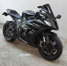 a black motorcycle parked in front of a white wall and cement floored area next to a building