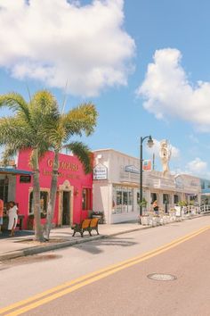 people are walking down the street in front of shops and palm trees on a sunny day