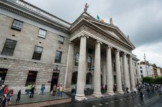 a large building with columns and flags on the top, along with people walking around