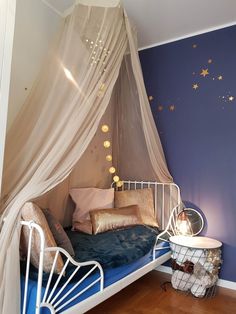 a white metal bed sitting in a bedroom next to a blue wall and wooden floors