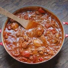 a pot filled with meat and vegetables on top of a wooden table next to a spoon