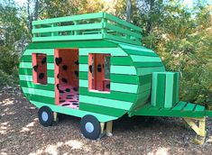 a green house made out of cardboard sitting on top of a dirt field next to trees