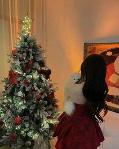 a woman in a red dress standing next to a christmas tree with lights on it