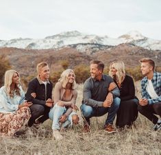 a group of people sitting on top of a grass covered field with mountains in the background