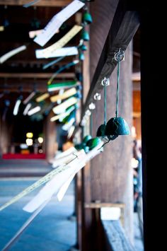 several bells hanging from the side of a wooden building with people walking in the background