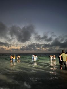 several people standing in the water at sunset or sunrise, with dark clouds above them