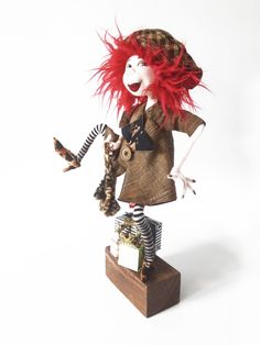 a doll with red hair is standing on top of a wooden block and holding two small stuffed animals