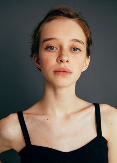 a woman with freckled hair and blue eyes poses for a photo in front of a gray background