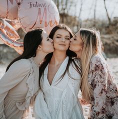 three beautiful women kissing each other on the beach with balloons in the air behind them