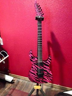 a pink zebra print guitar sitting on top of a stand next to a red wall