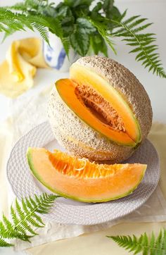 a melon cut in half on a plate next to some leaves and a potted plant