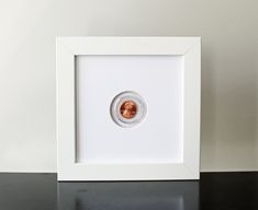 a white frame with a copper colored object in it on a black countertop next to a wall