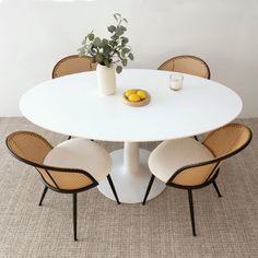 a white table with four chairs and a vase filled with lemons on the top