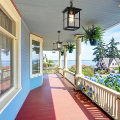 a porch with blue and white siding, light fixture hanging from the ceiling and potted plants on the railing