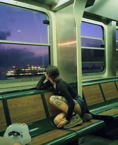 a woman sitting on top of a green bench next to a train window at night