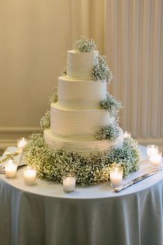 a white wedding cake sitting on top of a table covered in greenery and lit candles