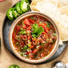 a bowl of salsa with tortilla chips on the side and green peppers in the background