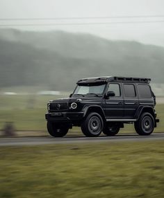 a black jeep driving down a road next to a lush green field