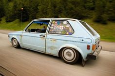 an old blue car with stickers on it's windshield driving down the road