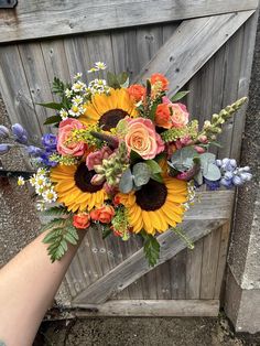 a person holding a bouquet of flowers in front of a wooden gate with an open door