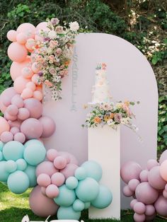 a wedding cake surrounded by balloons and flowers on the grass at a garden party in pastel colors