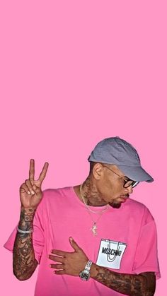 a man in a pink shirt and hat making the peace sign with his hand against a pink background