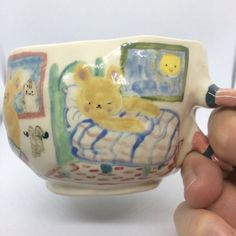 a hand holding a ceramic cup with a bear on it and other items around it