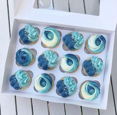 cupcakes with blue and white frosting in a box on a wooden table