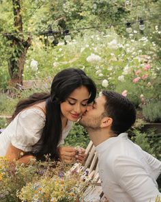 a man kissing a woman on the cheek while sitting in a chair surrounded by flowers