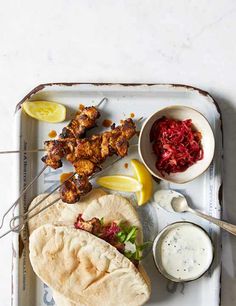 a tray with food on it including pita bread, sauces and lemon wedges