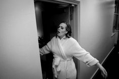 a woman in a bathrobe is standing by the door with her arms out