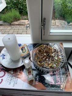 an assortment of jewelry on a table next to a candle and window sill in front of a glass door