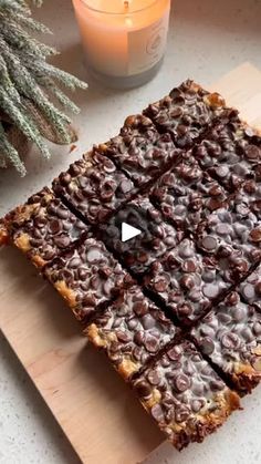 a wooden cutting board topped with brownies next to a candle